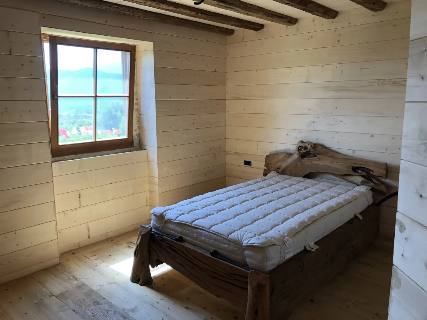 Camera da letto con testiera in radica e pareti rivestite in legno antico, finestra con vista sulle montagne