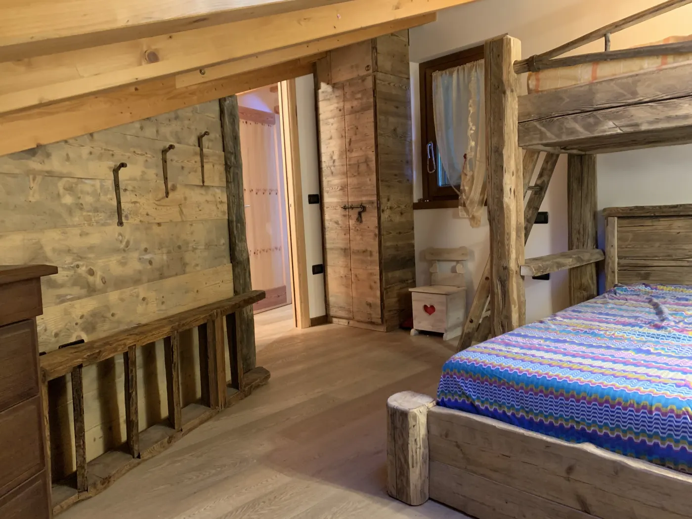 Camera con letto a soppalco e boiserie in legno antico, armadio su misura e appendiabiti in ferro battuto